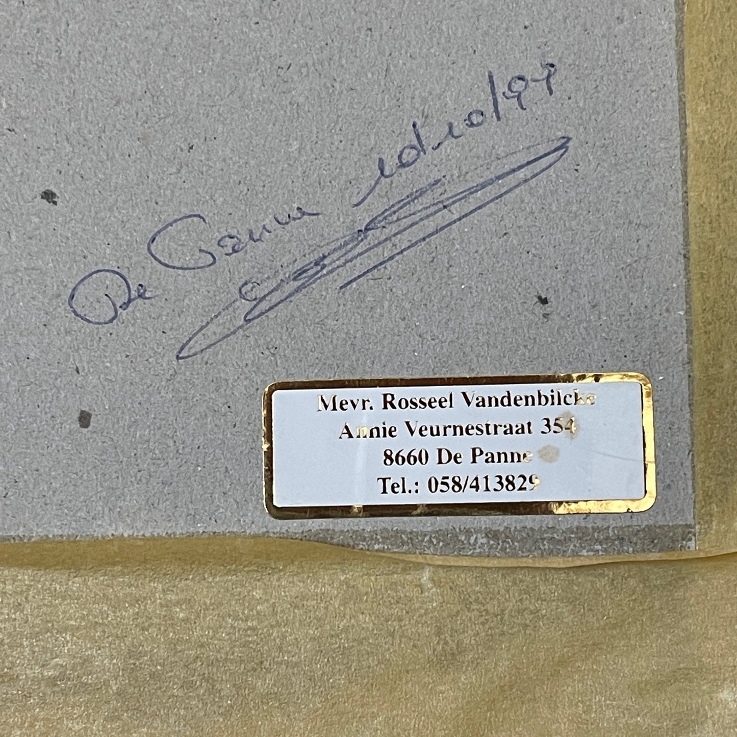 Signature on a textured surface with a gold border and contact information label.