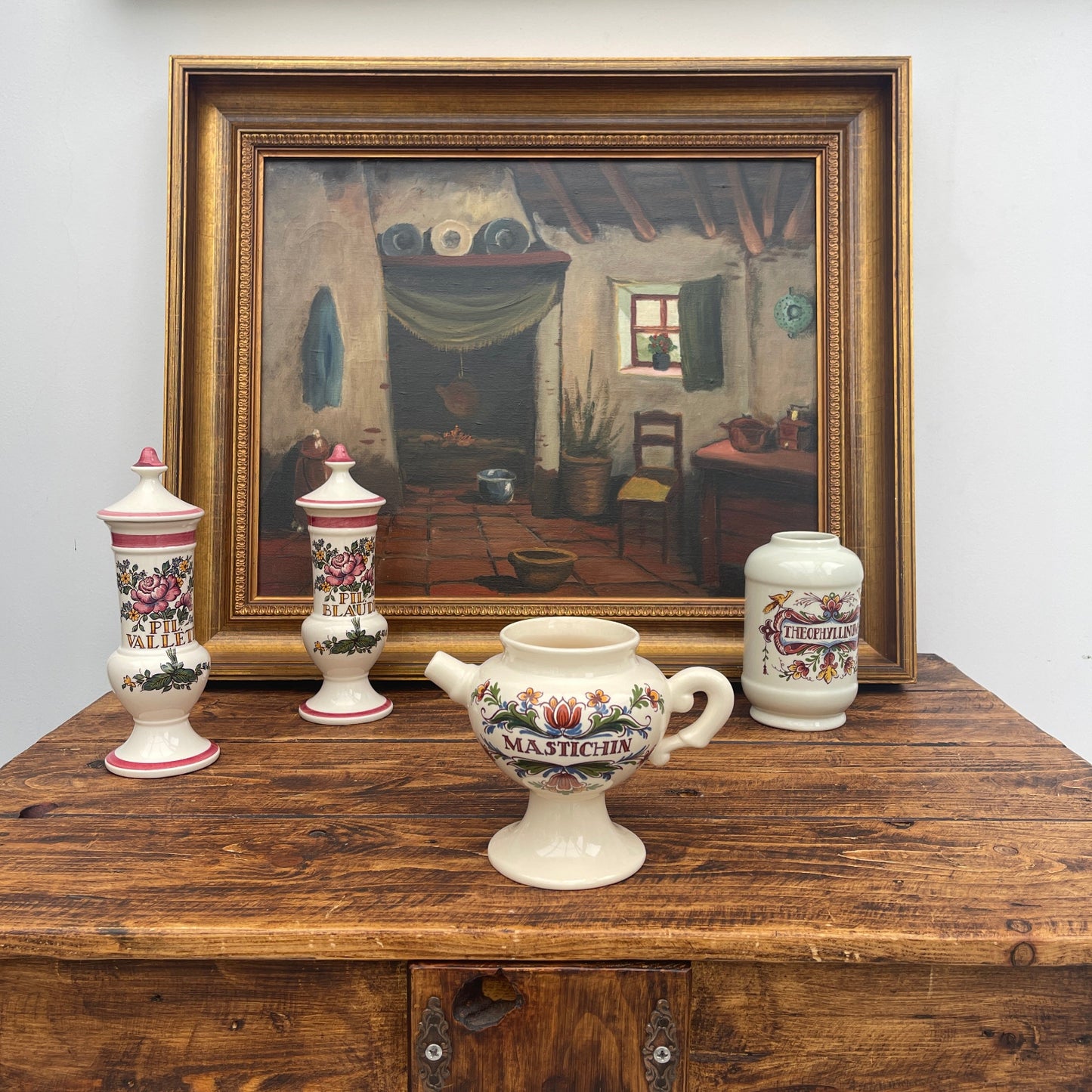 Decorative ceramic items on a wooden table with a framed painting in the background.