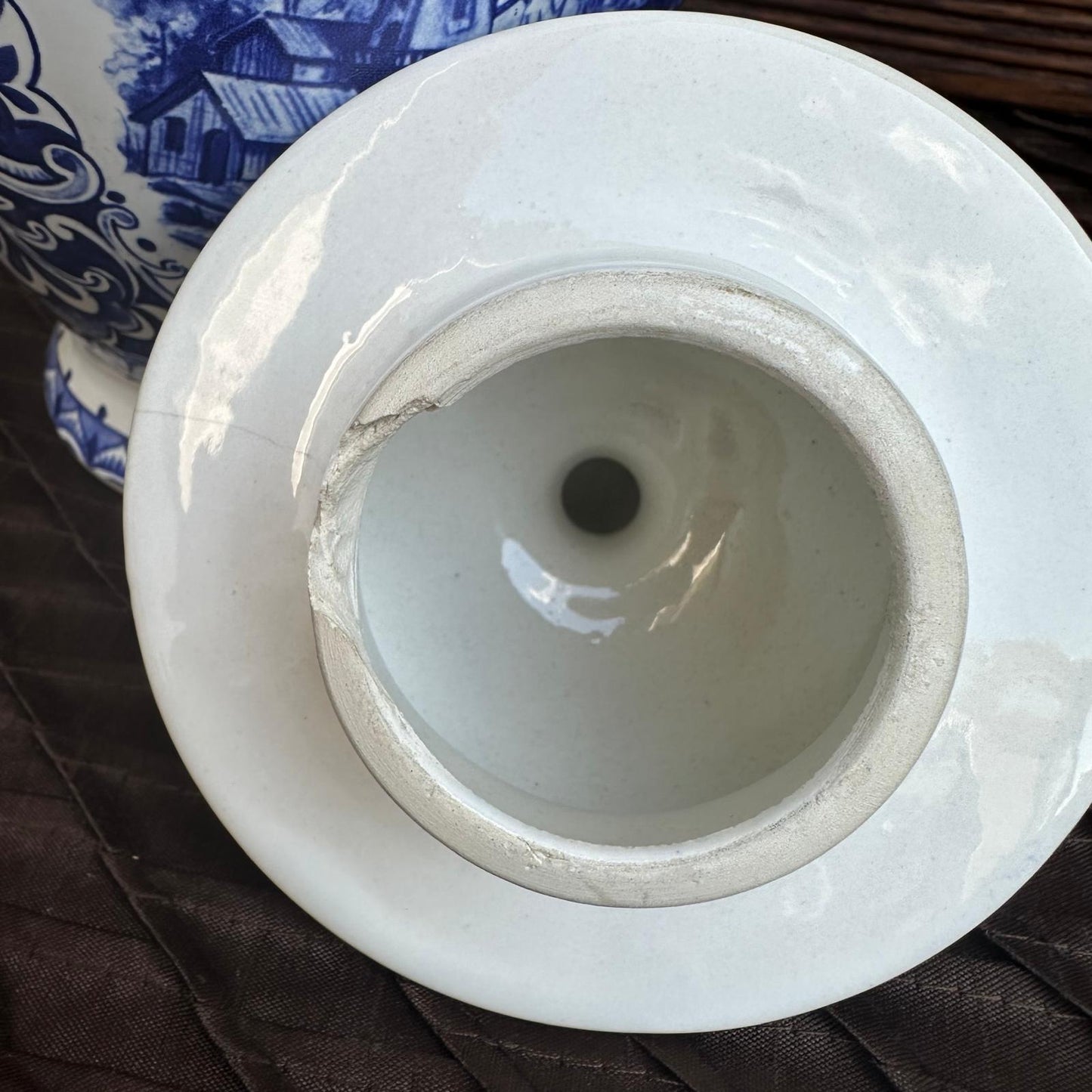 Close-up of a white ceramic vase with a blue patterned object in the background