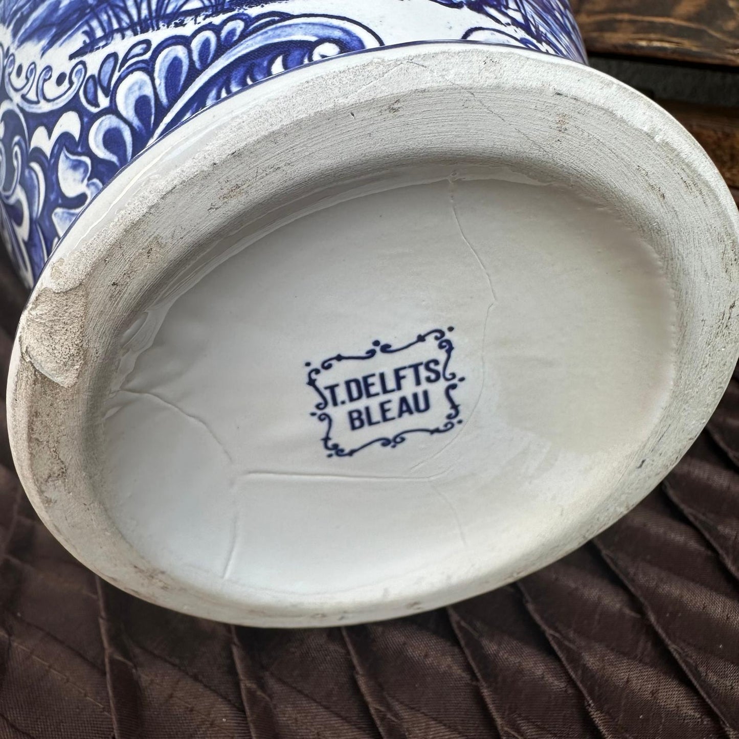 Vase with blue and white design and 'ST. Delfts Bleau' branding on a brown surface.