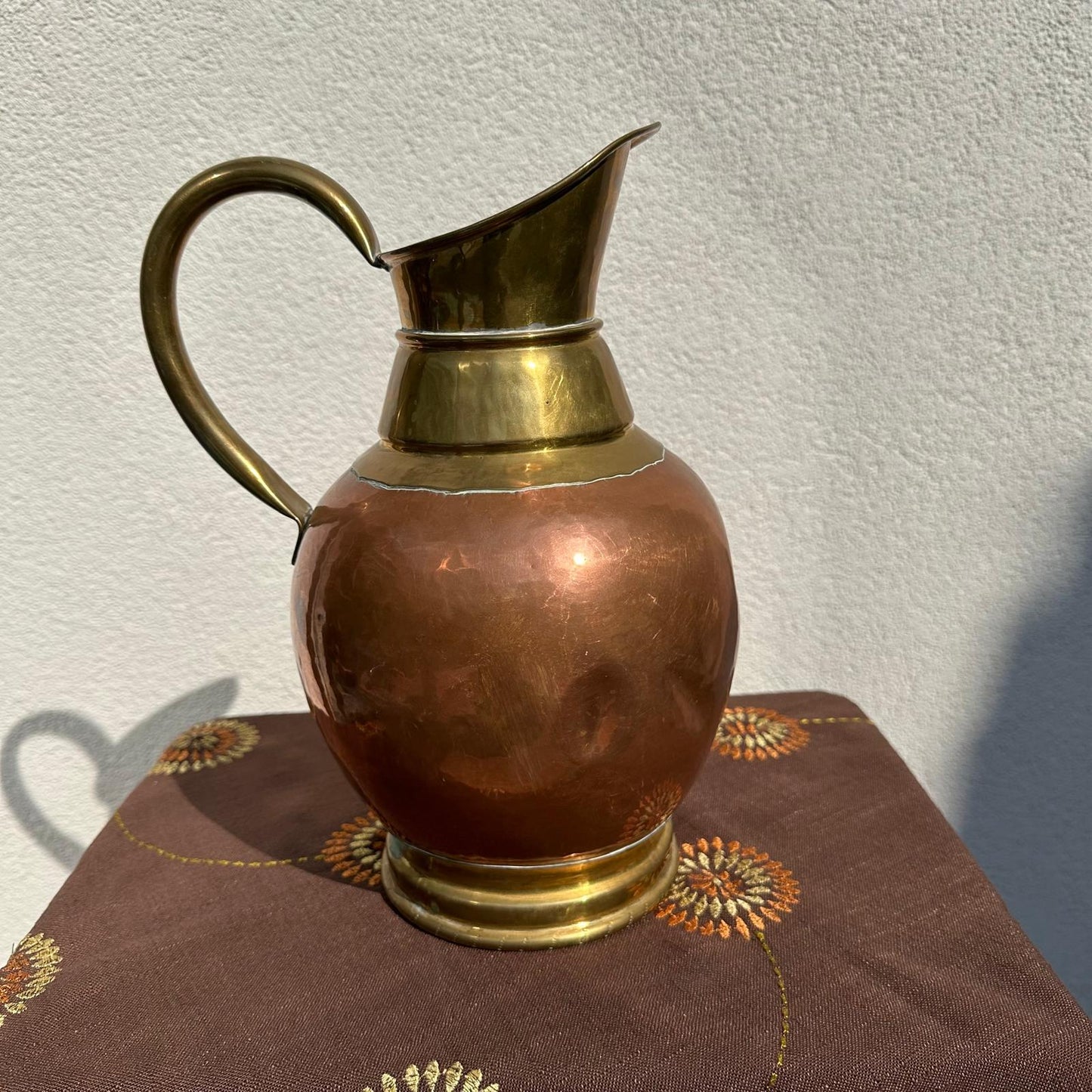 Copper and brass pitcher on a textured surface with a neutral background