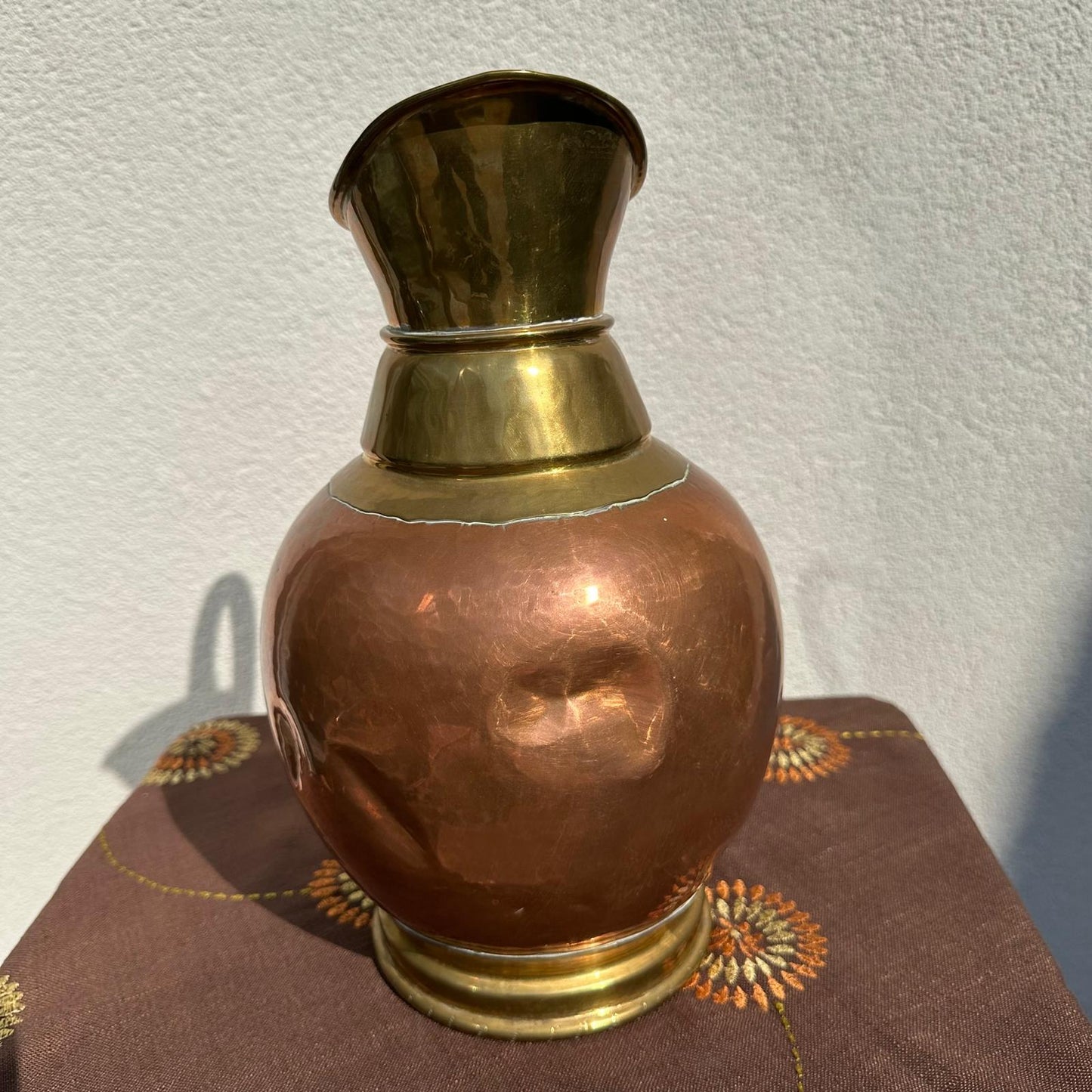 Copper and brass vase on a textured surface with a light background