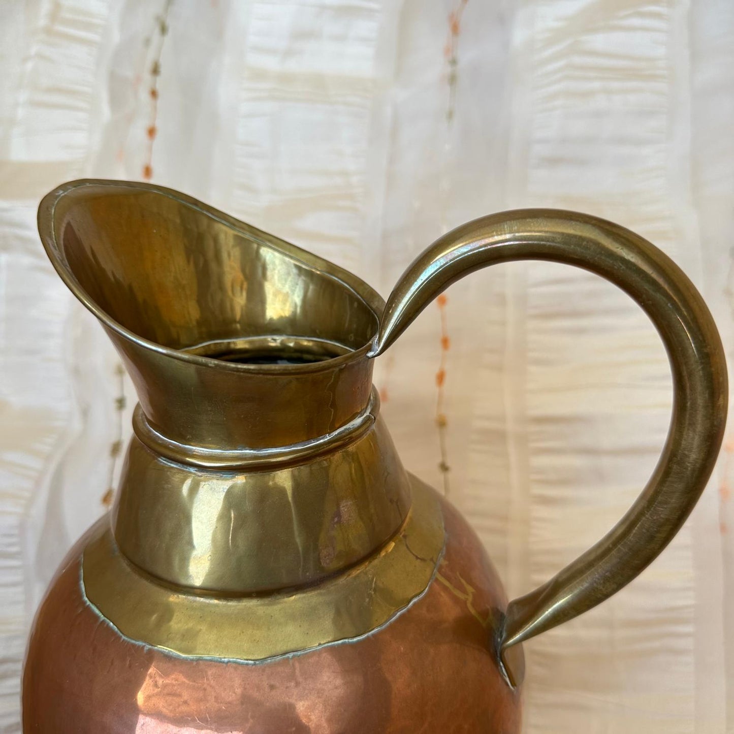 Brass and copper pitcher on a textured white background