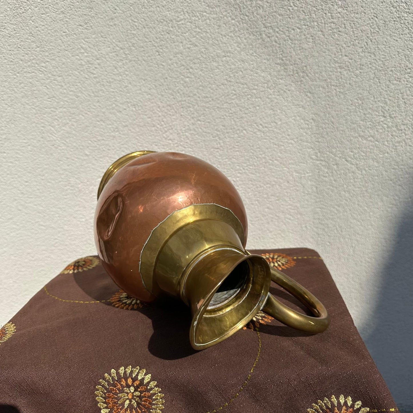 Copper and brass vase on a brown fabric with floral patterns