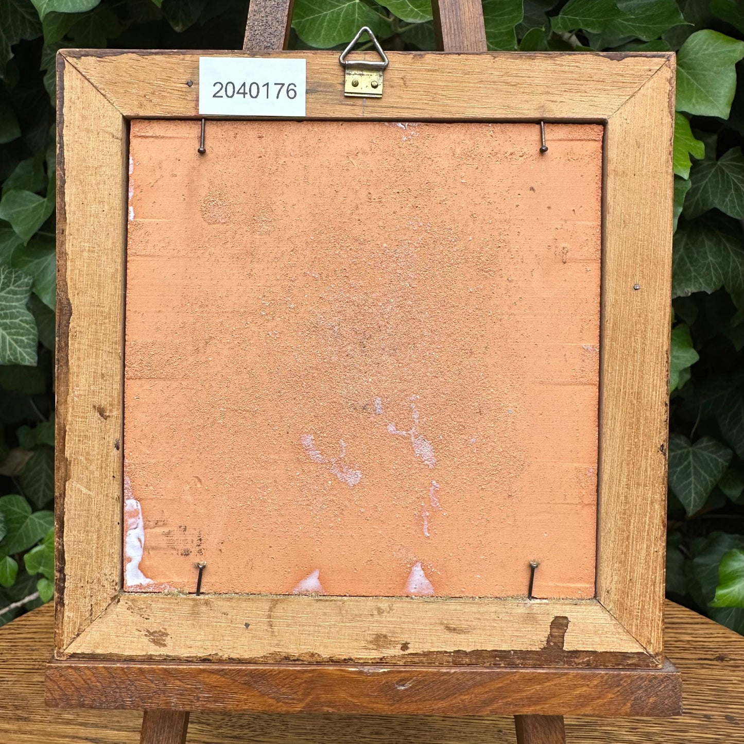 Wooden picture frame with a label on a wooden easel against a green leafy background