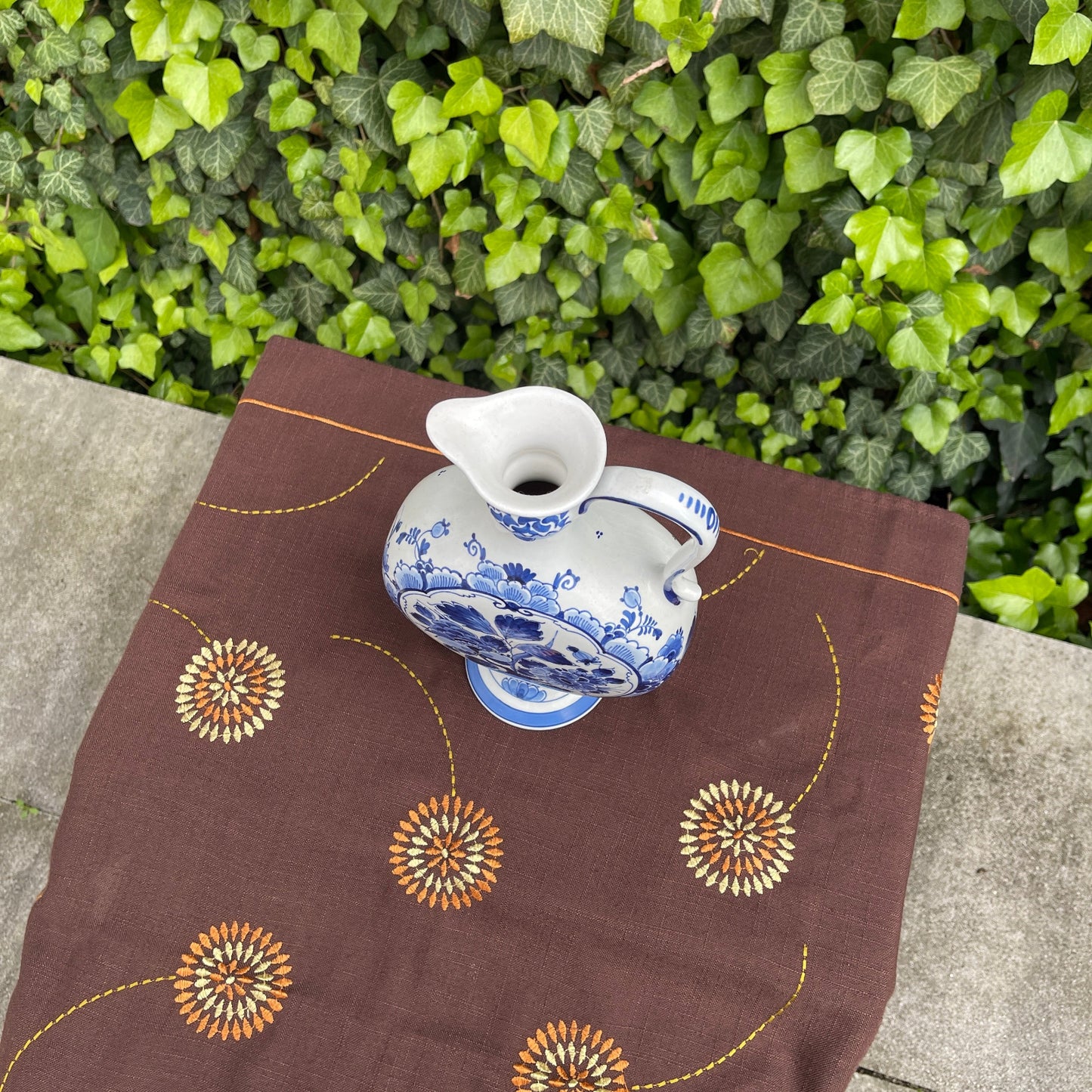 White ceramic teapot with blue floral patterns on a brown fabric with orange and green leafy background