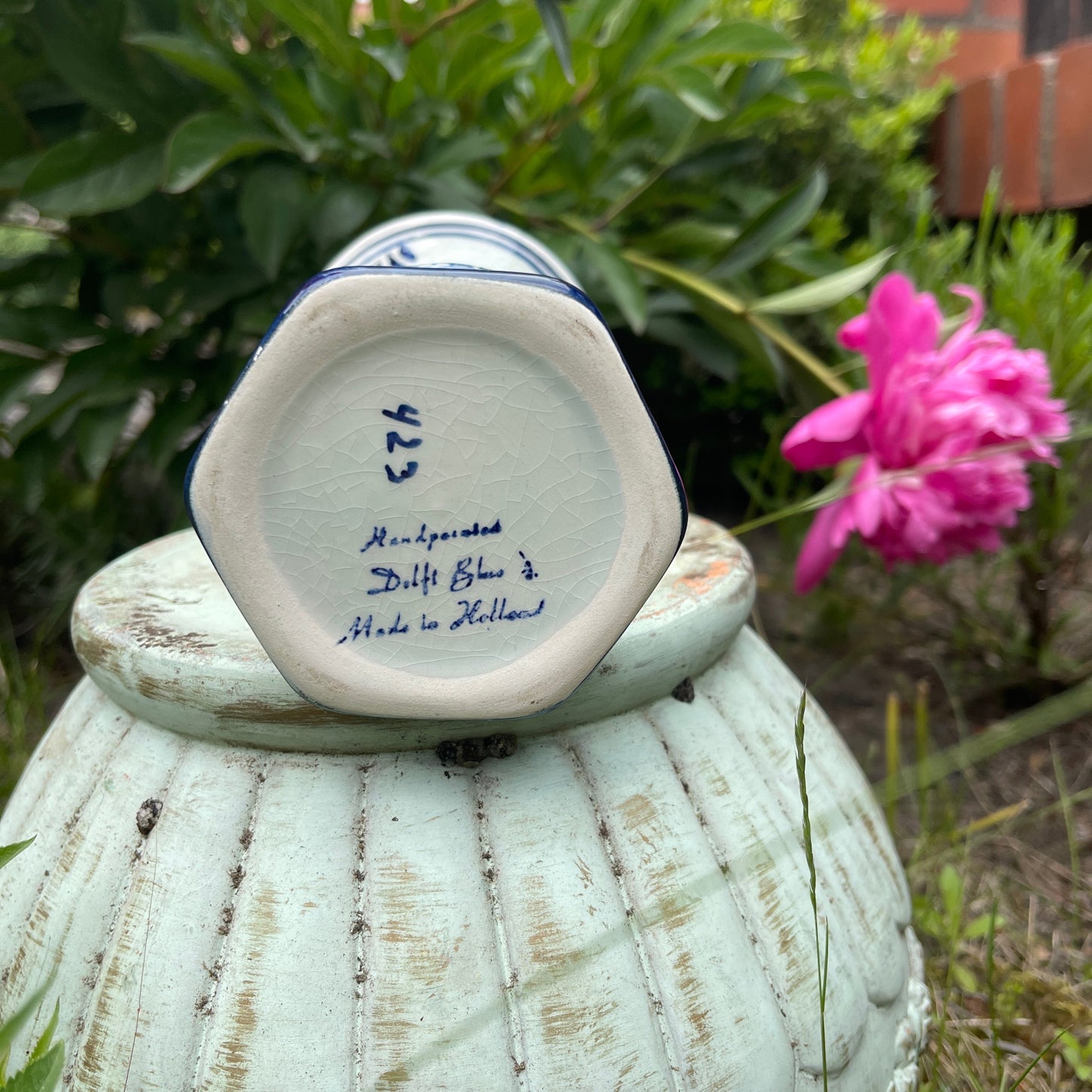 Ceramic vase with 'Delft Blue' marking on a textured surface with a pink flower in the background.