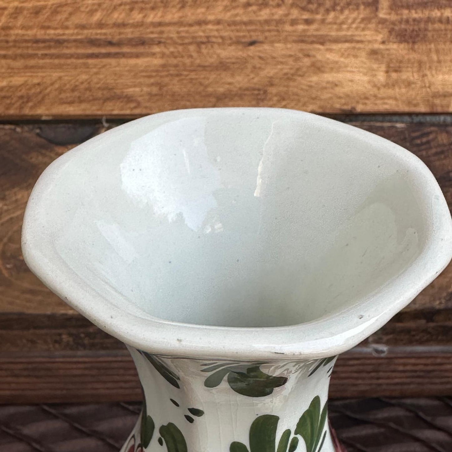 White ceramic vase with green floral patterns on a wooden surface