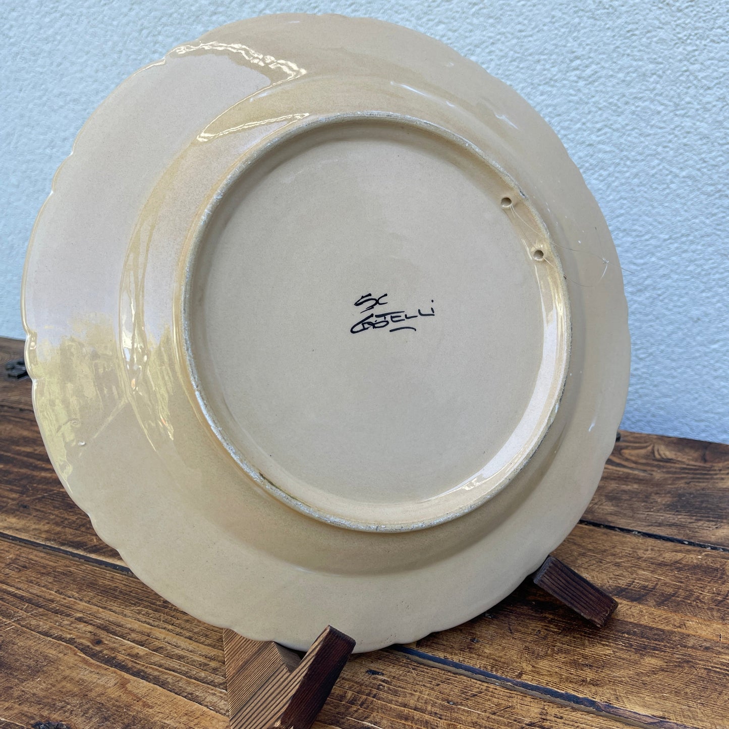 Ceramic plate with a signature on a wooden stand against a light blue wall.