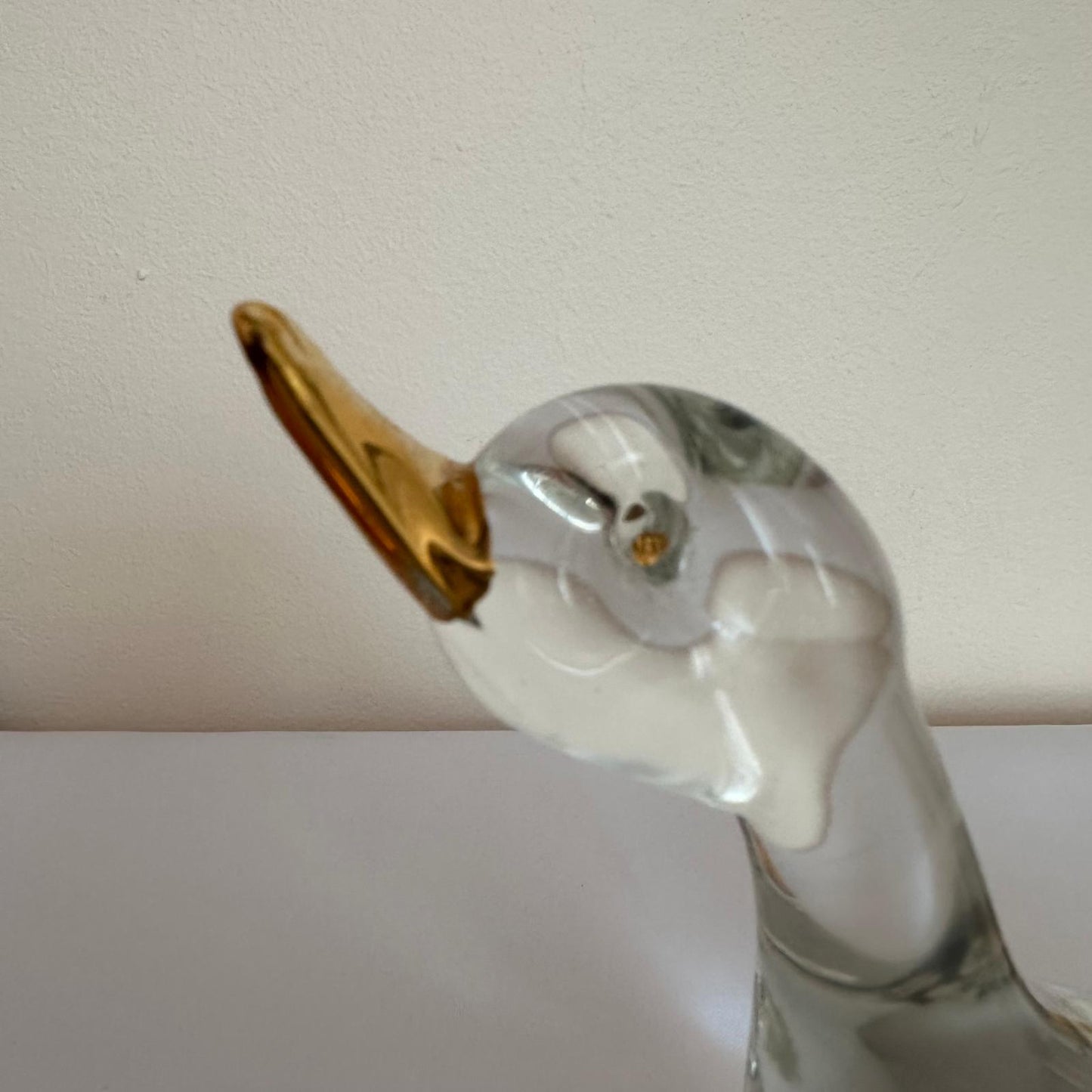 Glass duck figurine with a gold beak on a plain background