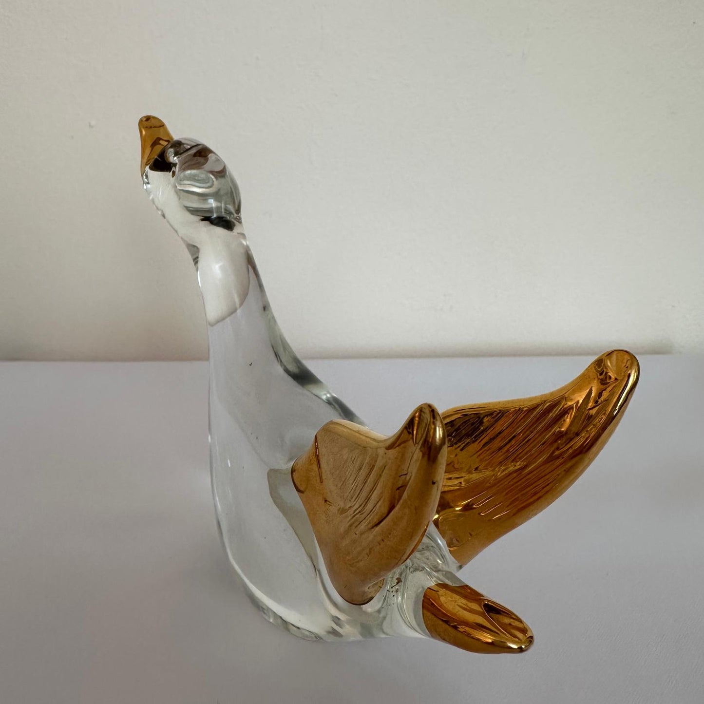 Glass sculpture of a bird with gold accents on a white surface