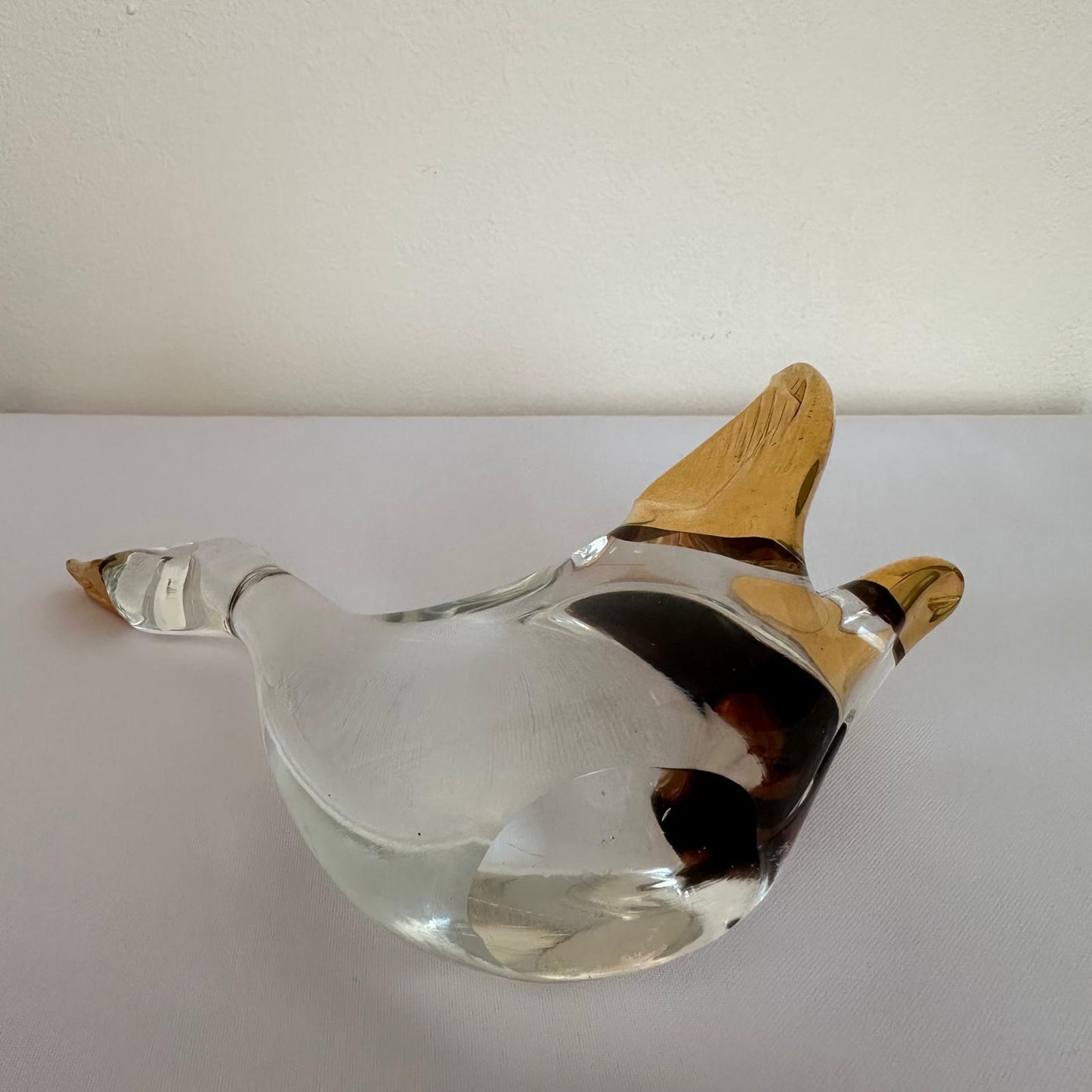Glass duck-shaped object with wooden beak on a white surface