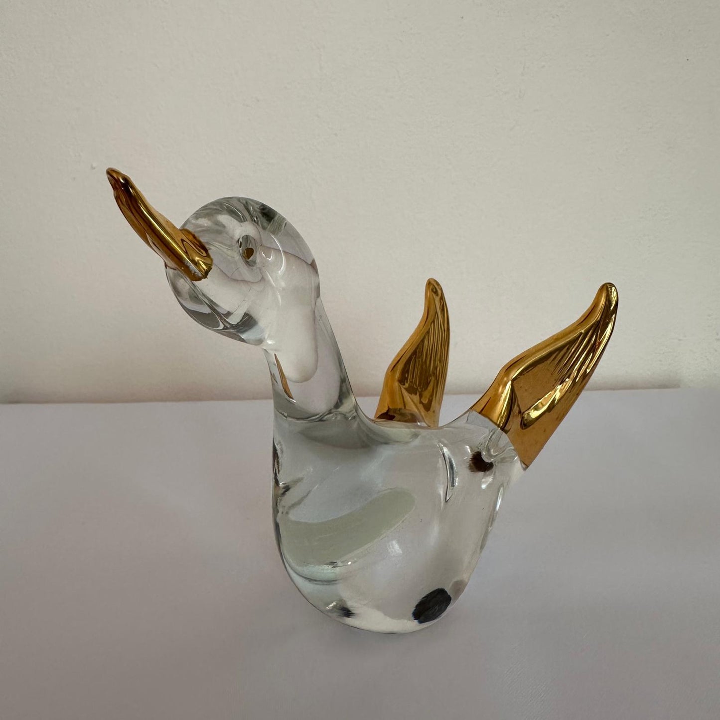 Glass duck figurine with gold wings on a white surface