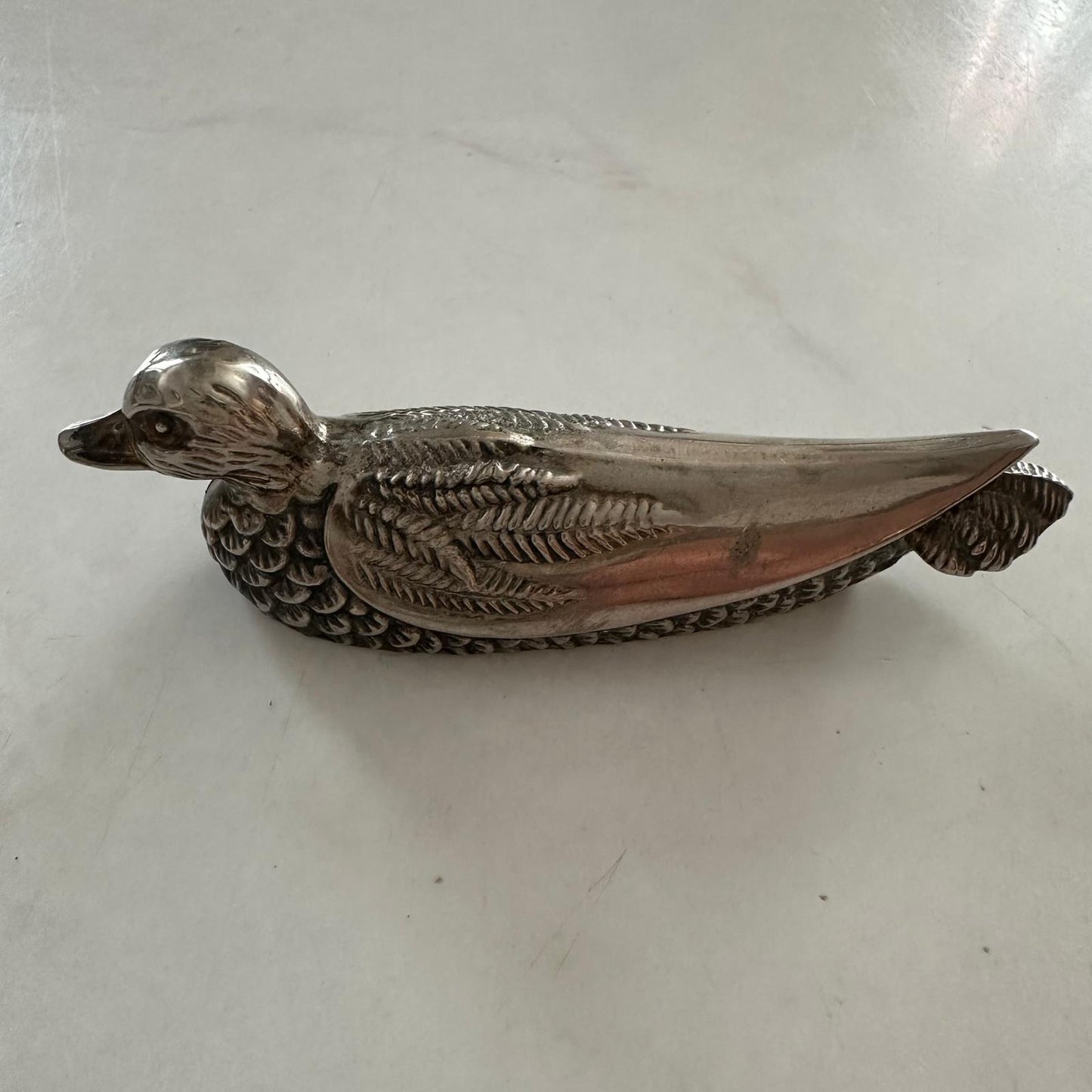 Silver duck-shaped object on a white surface