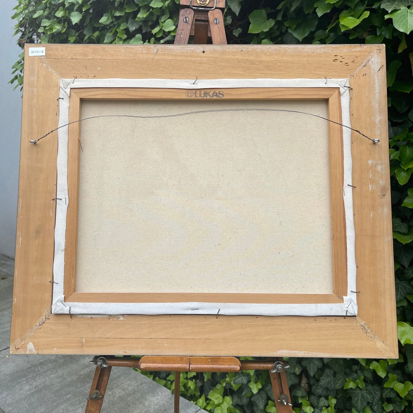 Empty canvas on an easel with 'Lukas' branding against a green leafy background