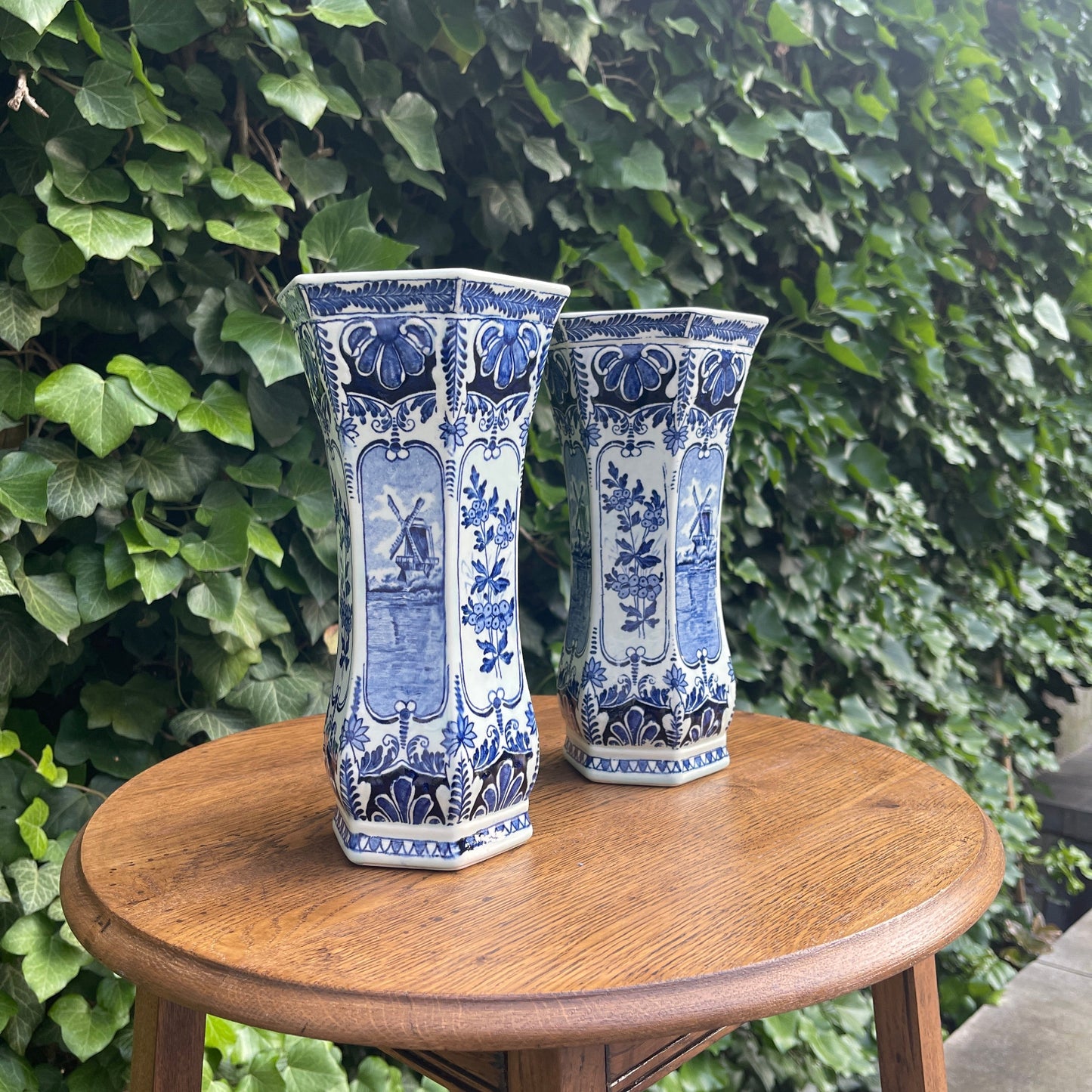 Two blue and white vases on a wooden table with a green leafy background