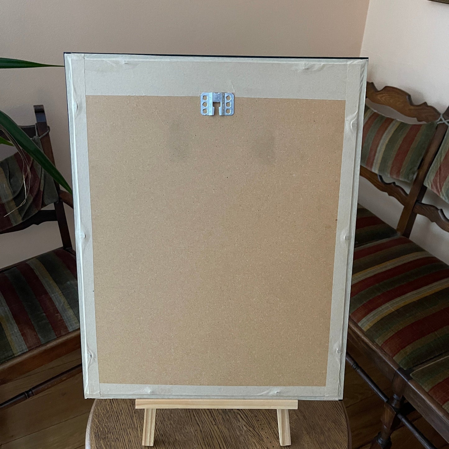 Beige cork bulletin board with wooden frame on a stand in a room with striped furniture.