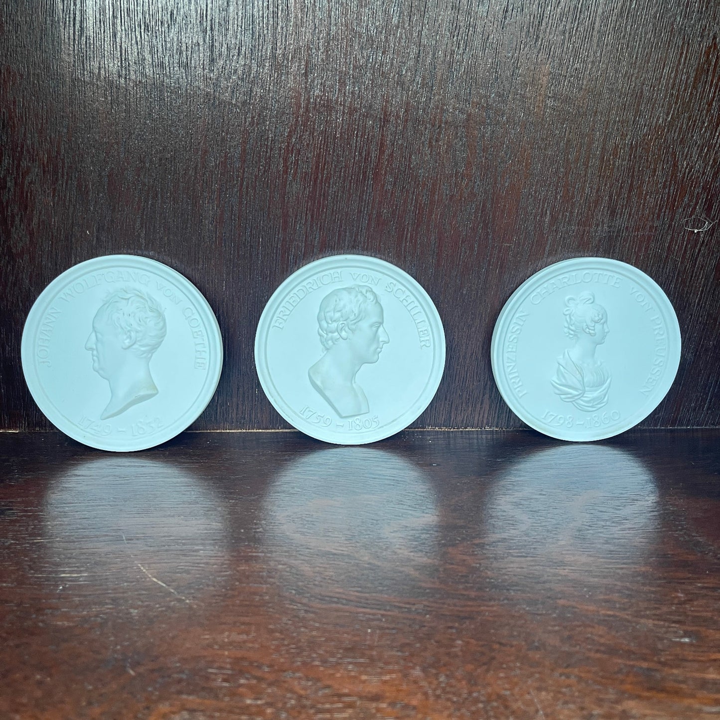 Three light blue coins with embossed portraits on a dark wooden surface