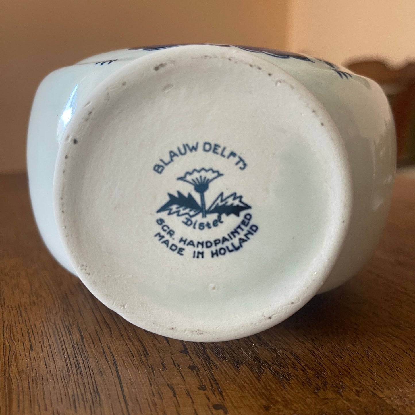 Back of a ceramic vase with 'Blauw Delft' branding on a wooden surface