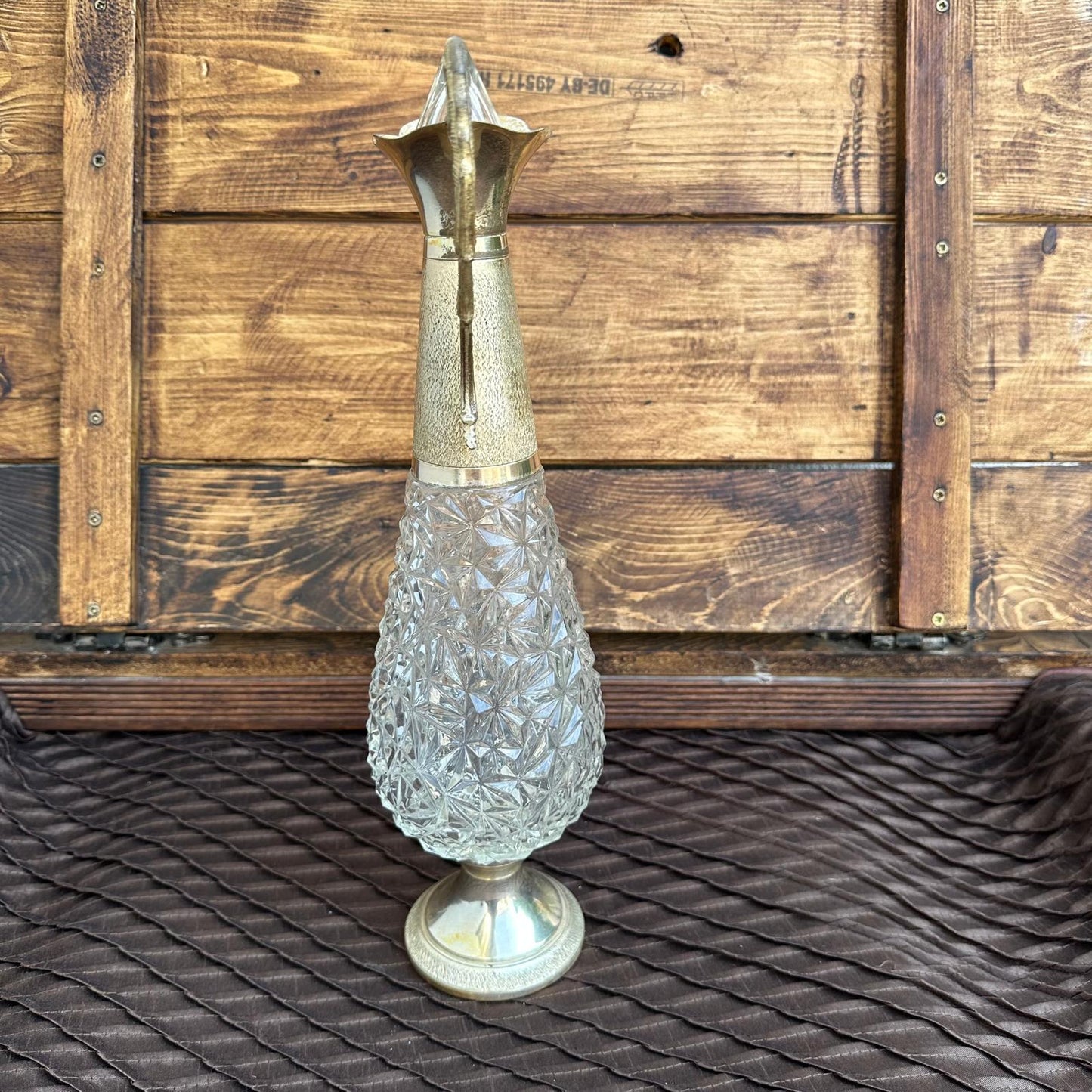 Decorative glass vase with metallic top on a textured surface with wooden background