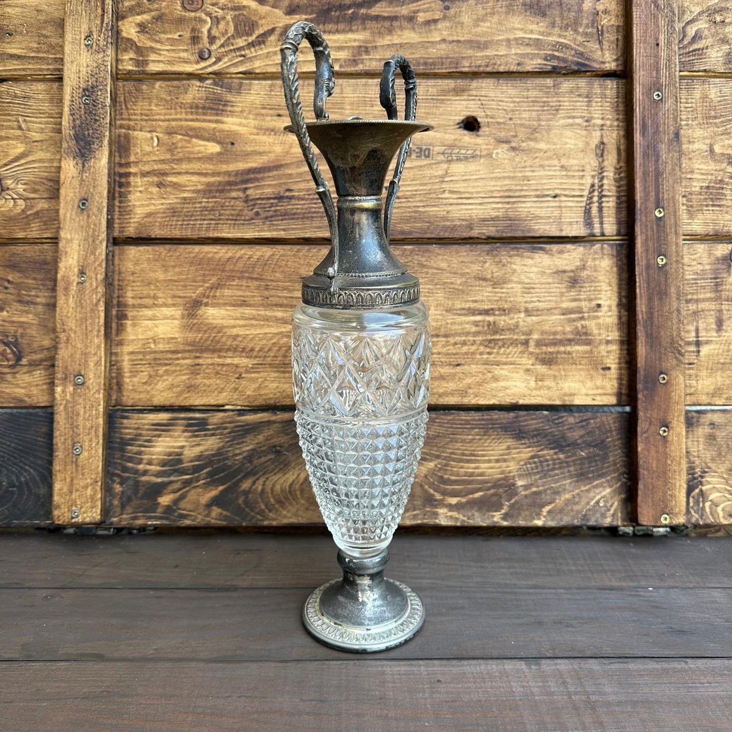 Decorative vase with glass body and metal top against a wooden background