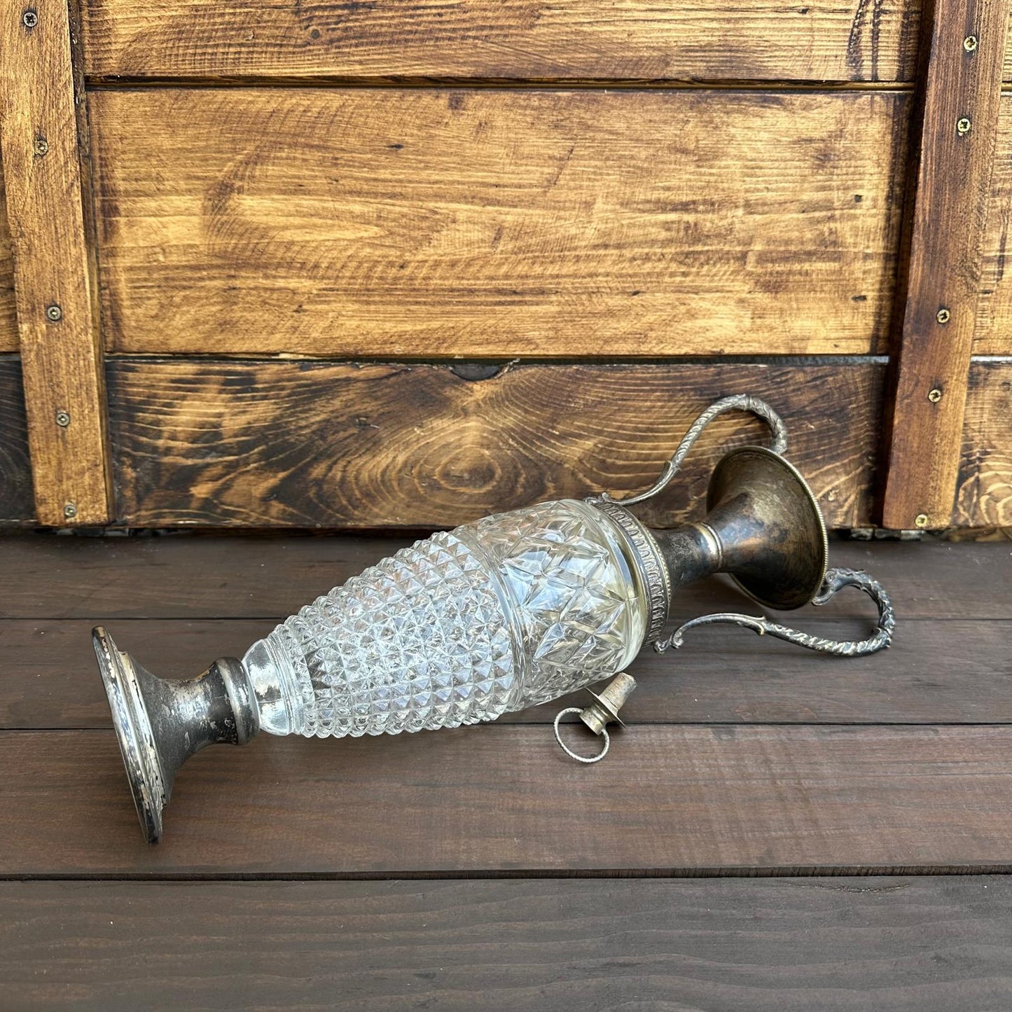 Decorative glass and metal vase on a wooden surface with a wooden crate in the background