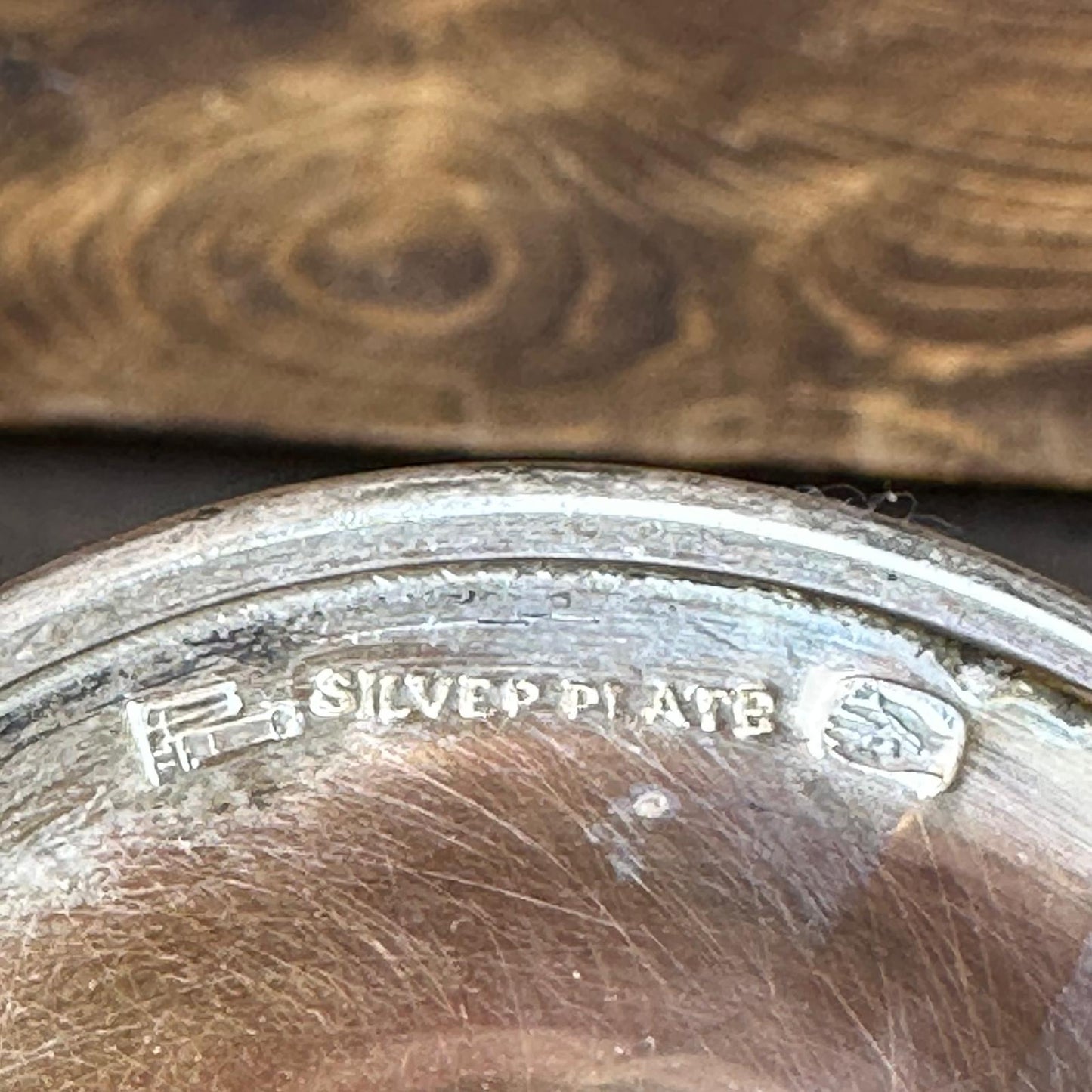 Close-up of a silver plate with 'SILVER PLATE' engraving on a wooden surface.