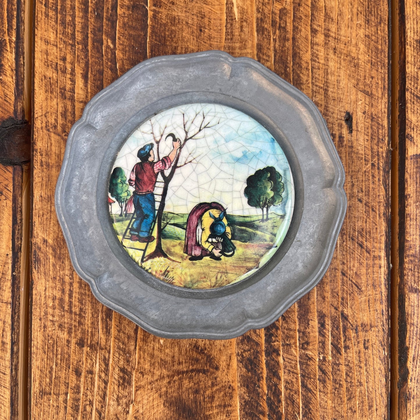 Decorative plate with a scenic design of people and trees on a wooden surface