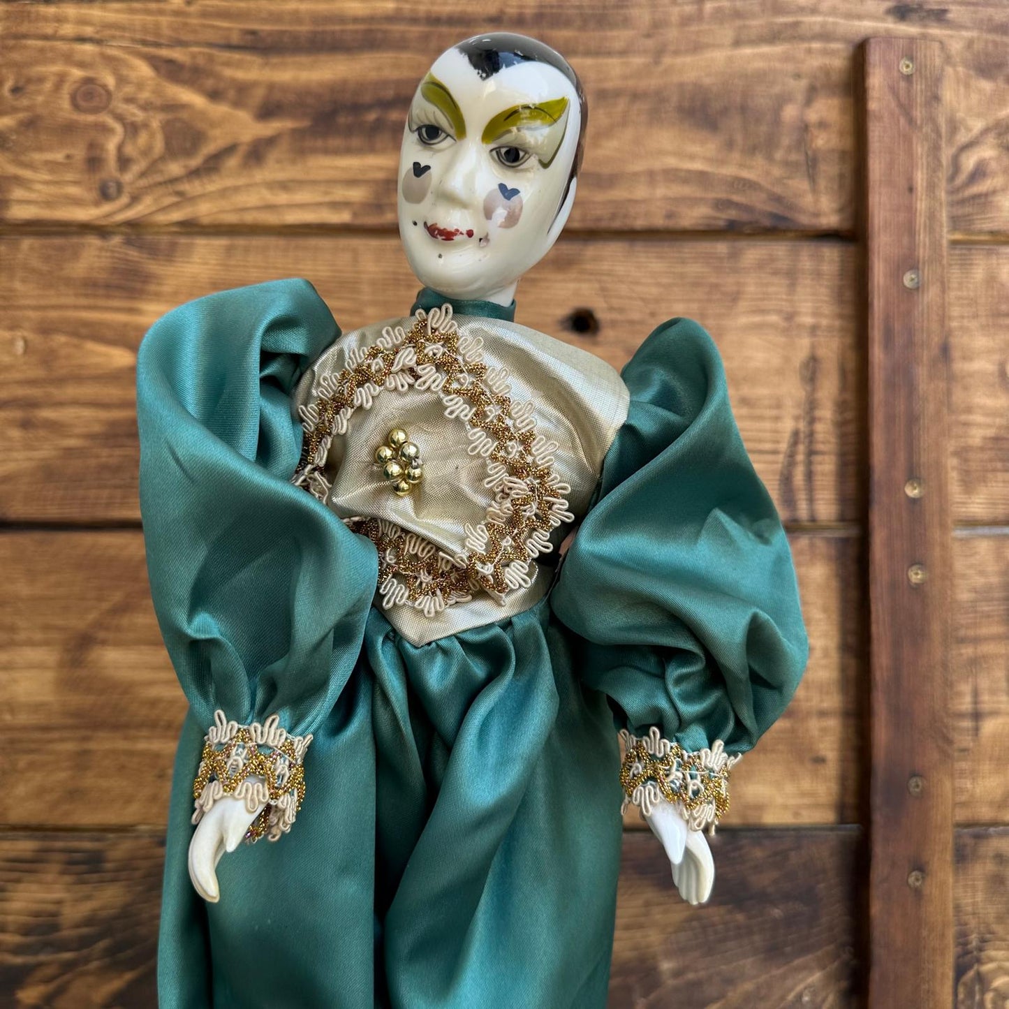 Decorative doll with teal dress and gold accents against a wooden background