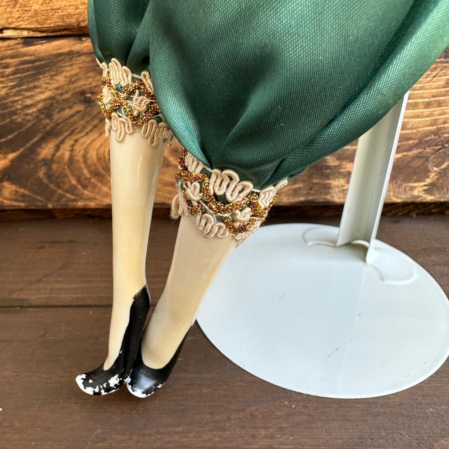 Doll with green dress, gold shoes, and decorative elements on a wooden surface