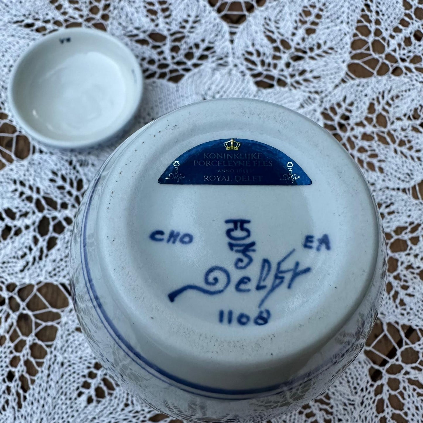 Ceramic container with blue text and a smaller bowl on a lace tablecloth