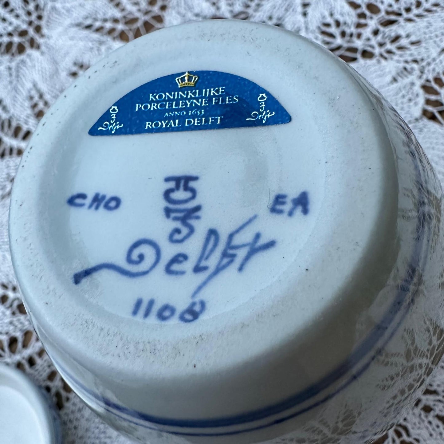 Close-up of a Royal Delft ceramic item with branding and signature on a lace tablecloth.