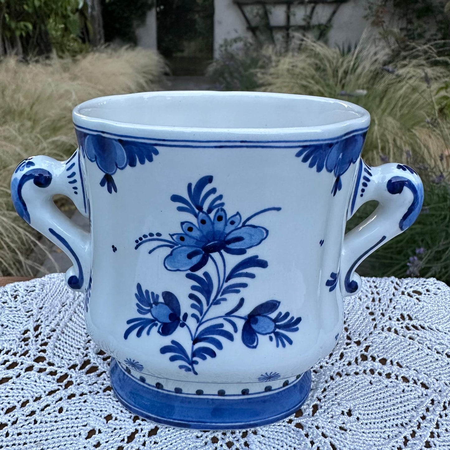 White ceramic mug with blue floral patterns on a lace tablecloth outdoors.