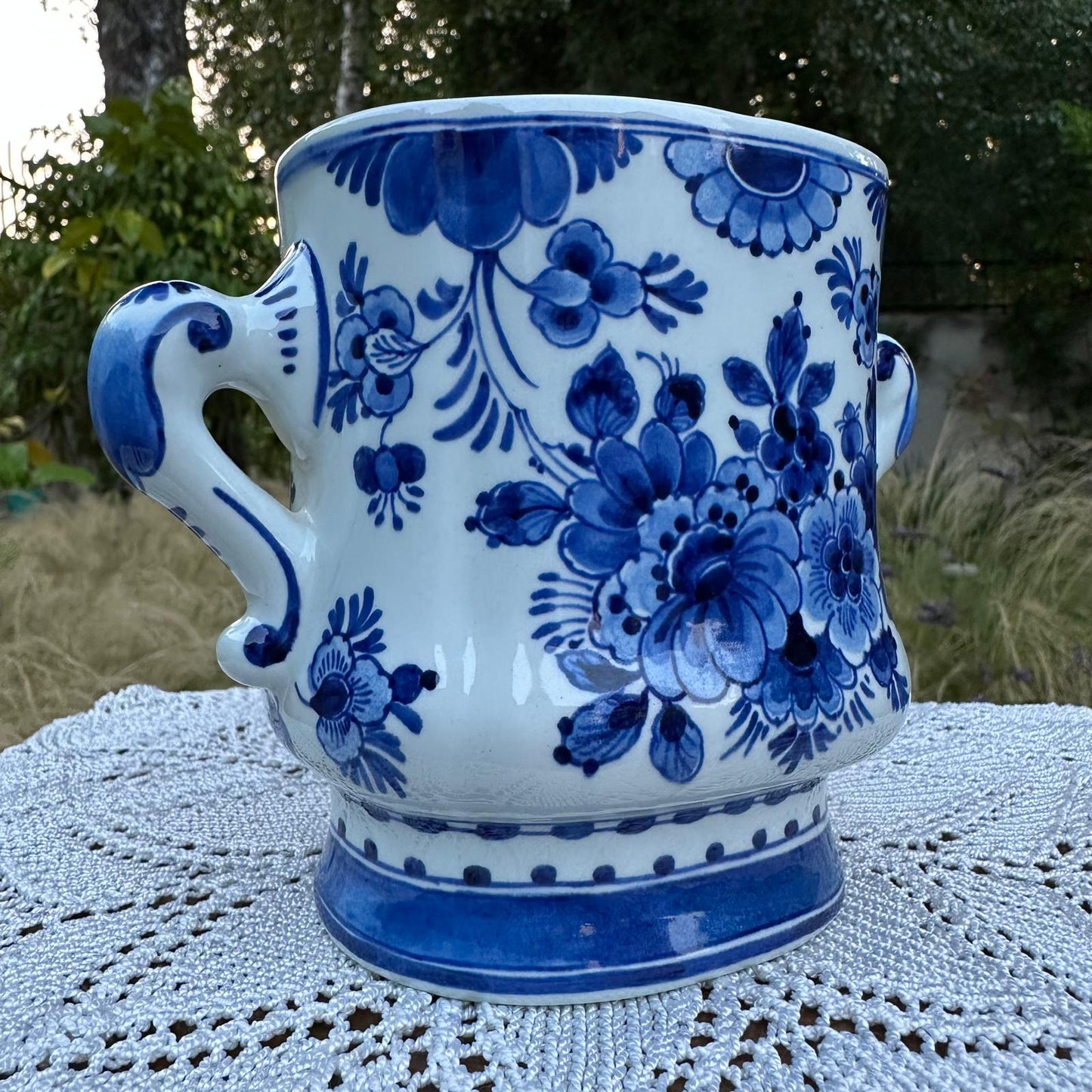 Ceramic mug with blue floral patterns on a white lace tablecloth outdoors.