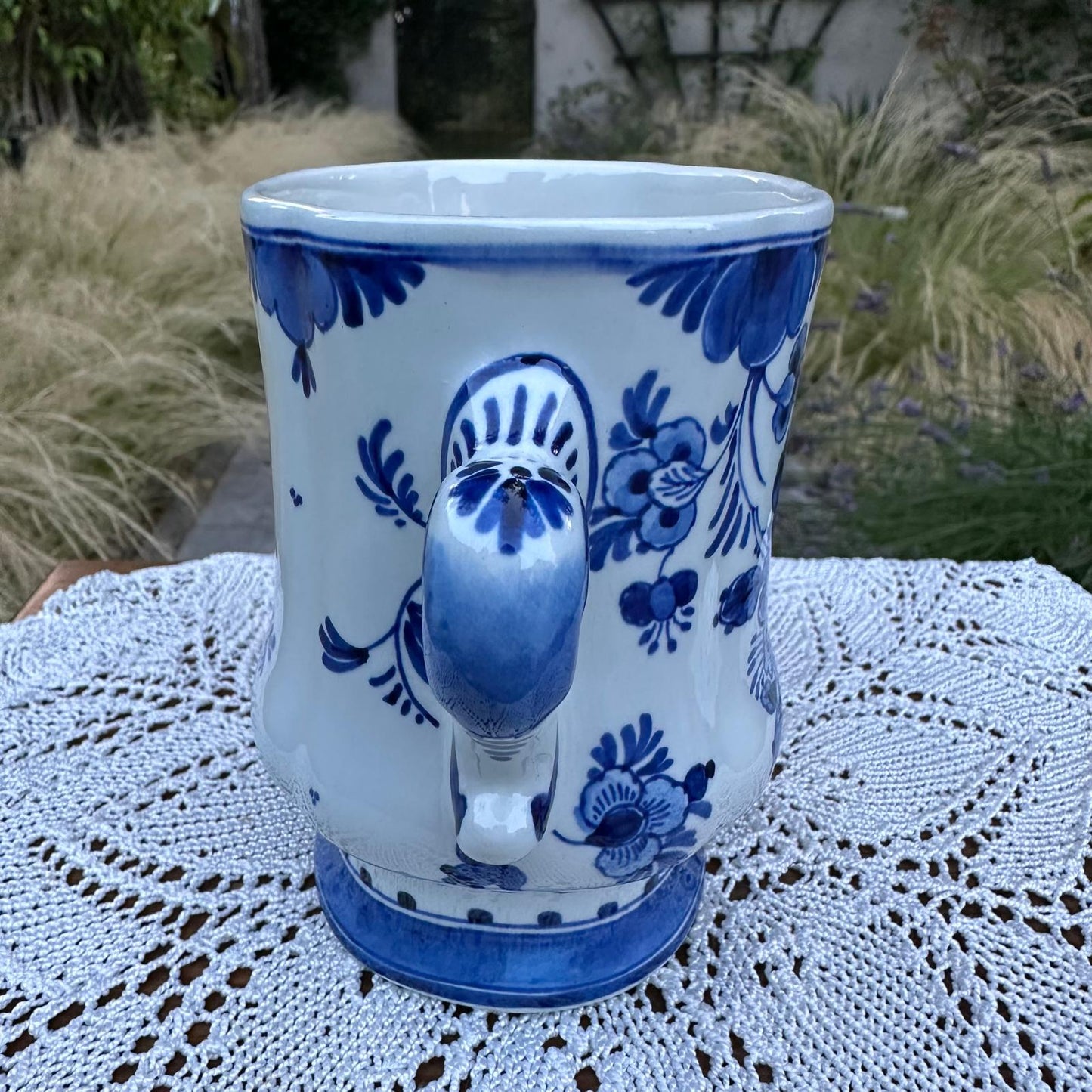 Blue and white ceramic mug with floral patterns on a lace tablecloth outdoors.