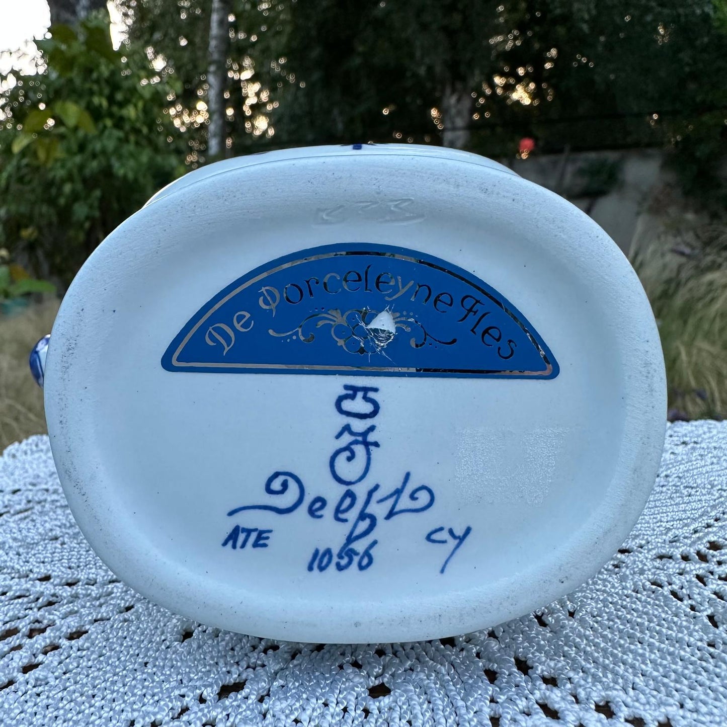 White ceramic item with blue text and logo on a textured surface with greenery in the background