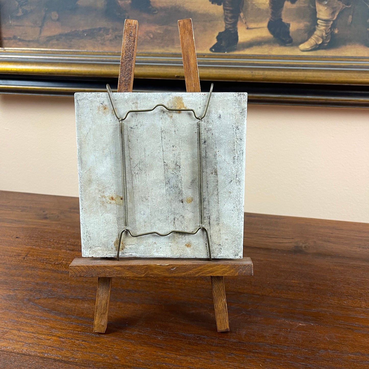 Vintage metal mousetrap on a wooden stand with a framed picture in the background