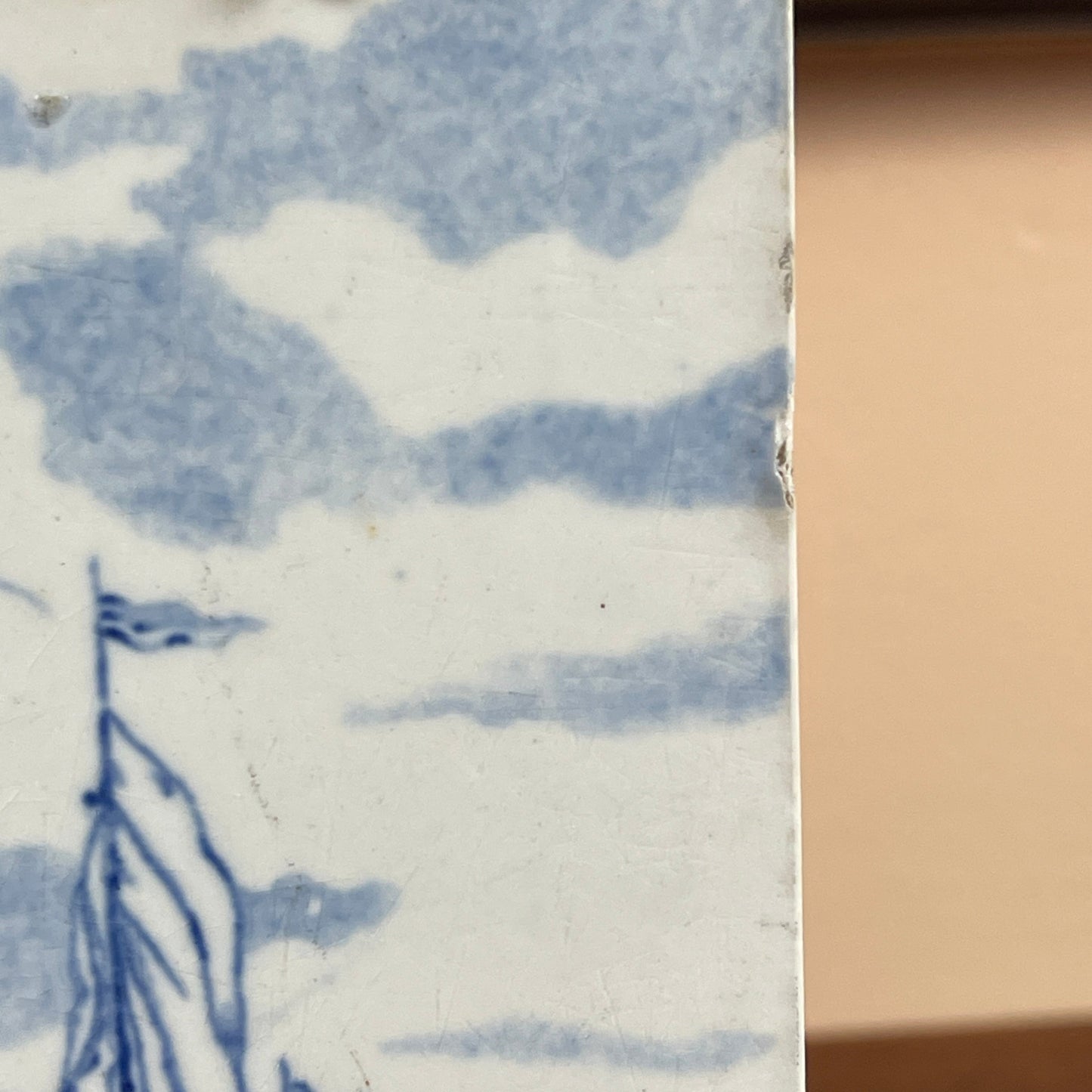 Close-up of a ceramic tile with blue and white design, featuring a landscape scene.