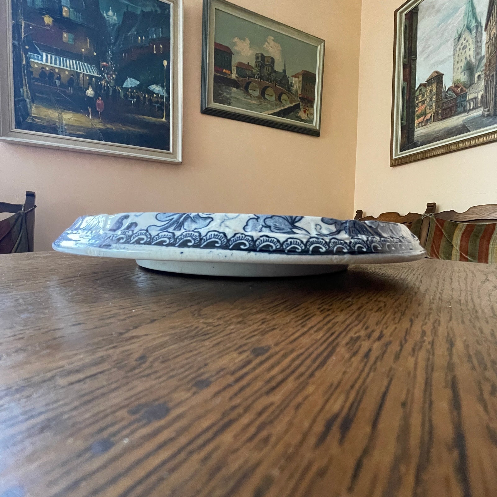 Blue and white ceramic plate on a wooden table with framed pictures on the wall.