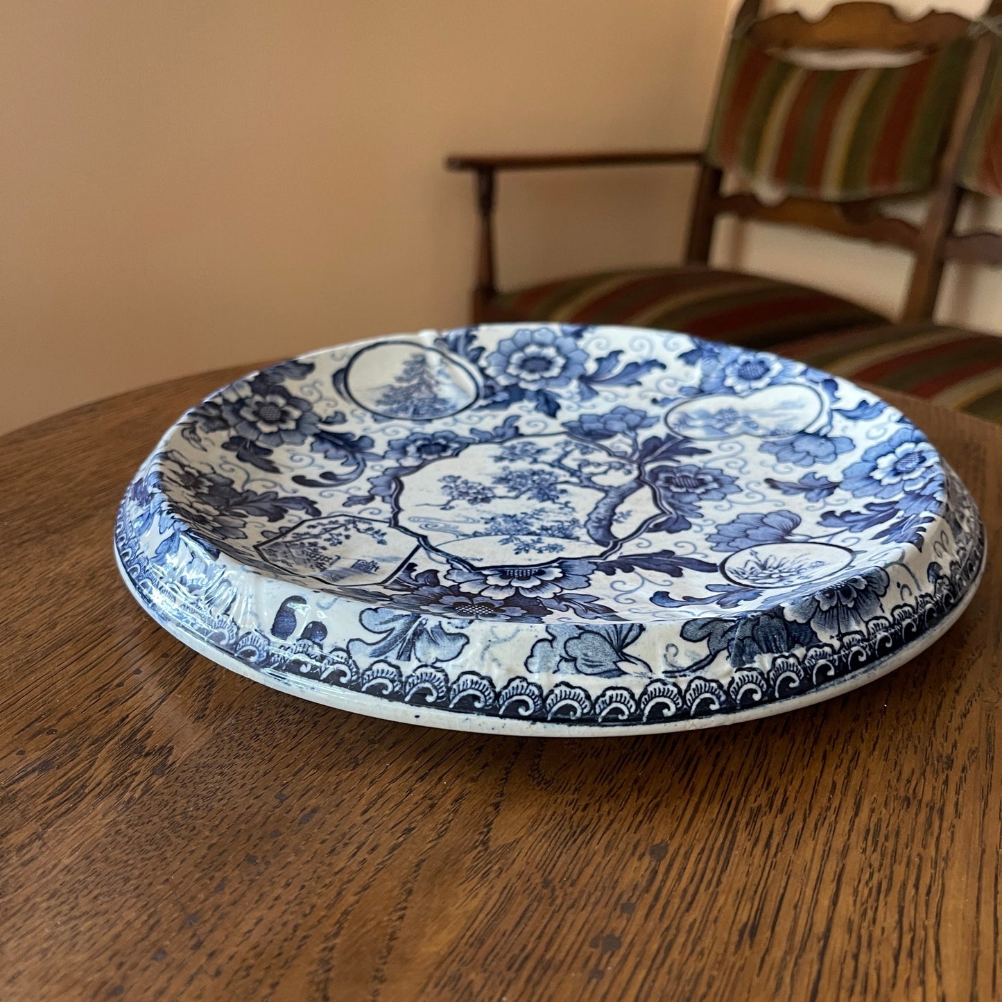 Blue and white floral-patterned plate on a wooden table with a chair in the background.