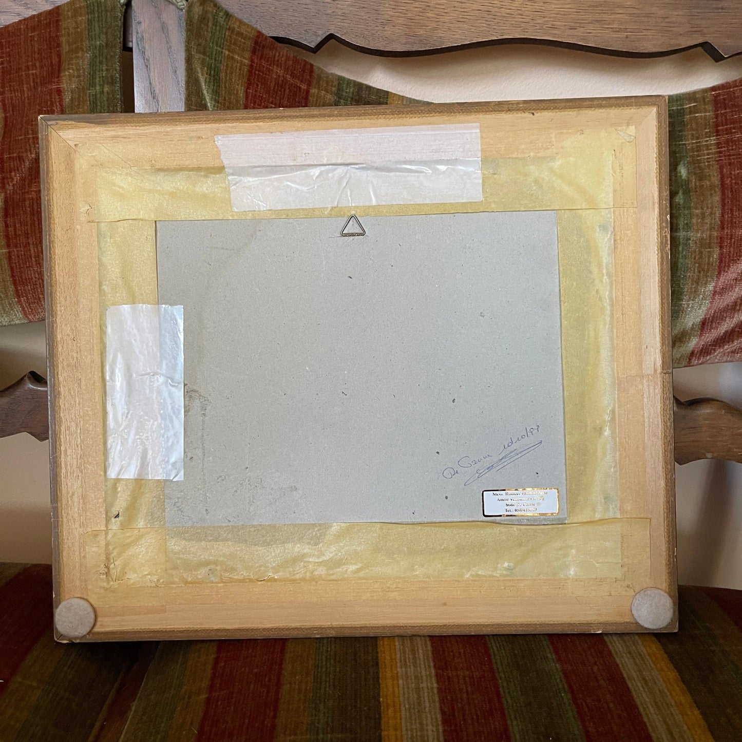 Back view of a wooden picture frame with a white mat and glass on a striped fabric background.