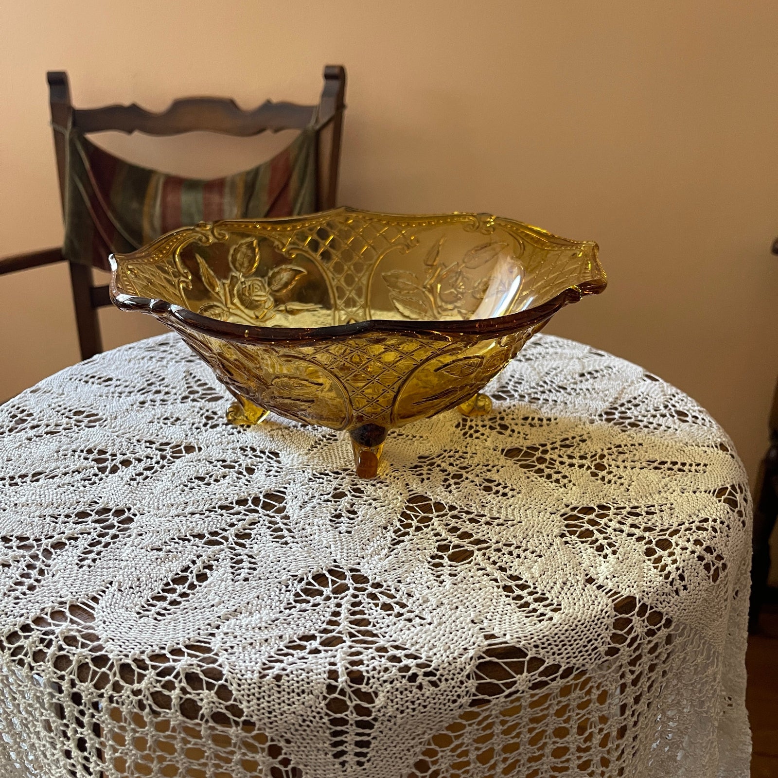 Decorative gold bowl on a lace tablecloth with a wooden chair in the background.