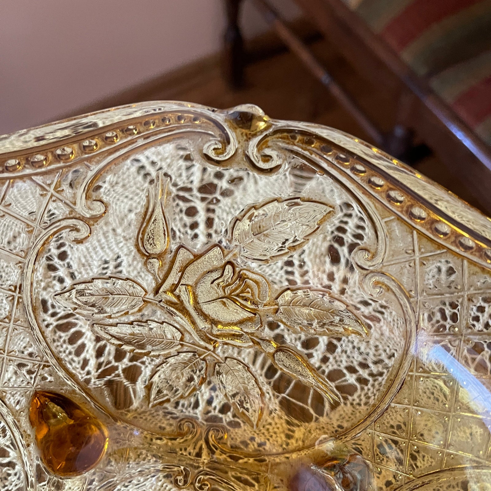 Decorative glass dish with floral engraving and amber-colored stones on a wooden surface.