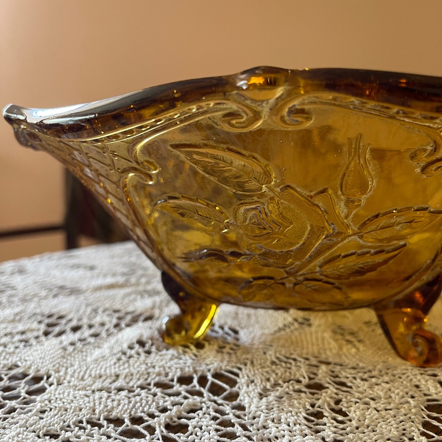 Decorative amber glass bowl with floral patterns on a lace tablecloth.
