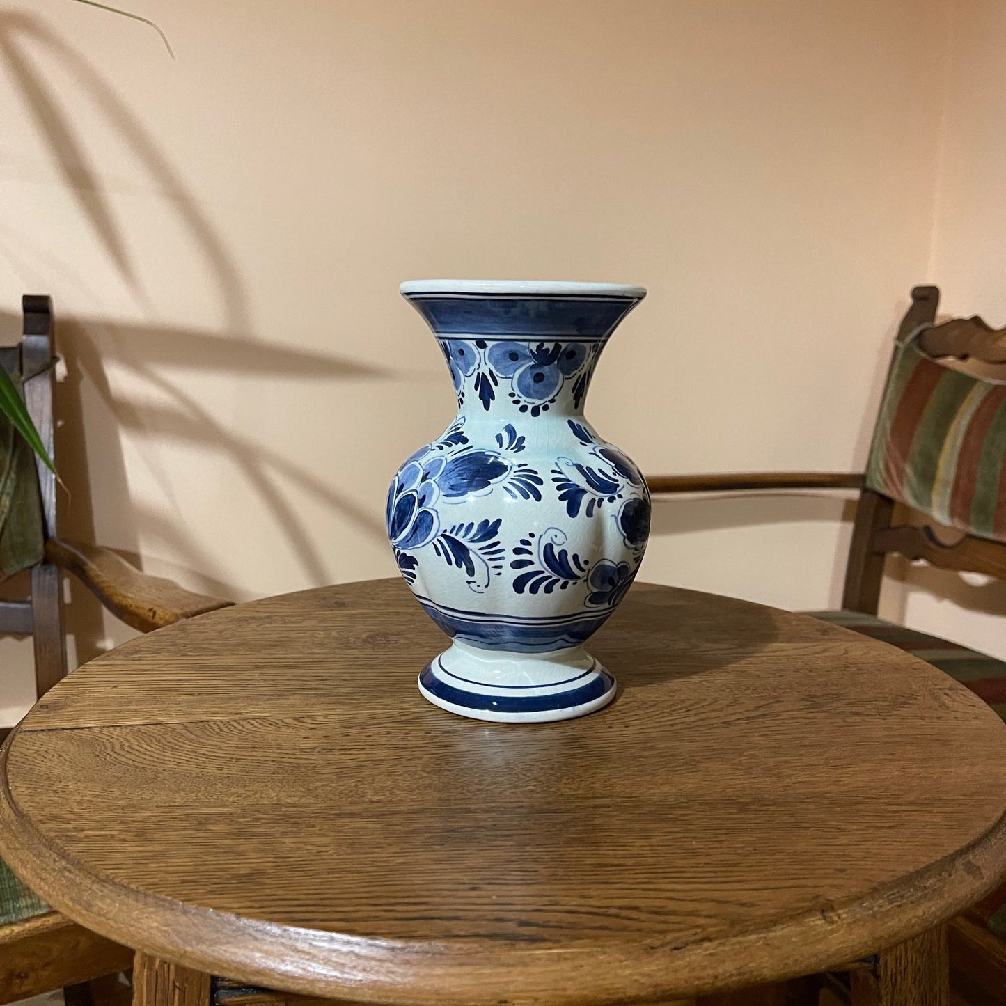 Blue and white floral-patterned vase on a wooden table with chairs in the background
