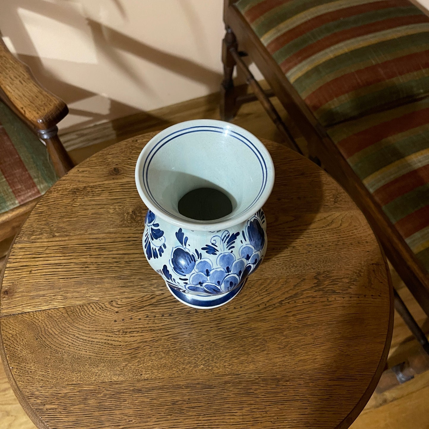 Blue and white ceramic vase on a wooden table with striped chairs in the background