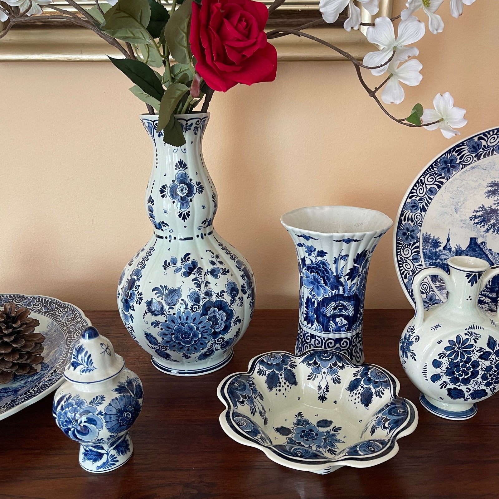 Collection of blue and white ceramic pieces on a wooden surface with flowers in the background.