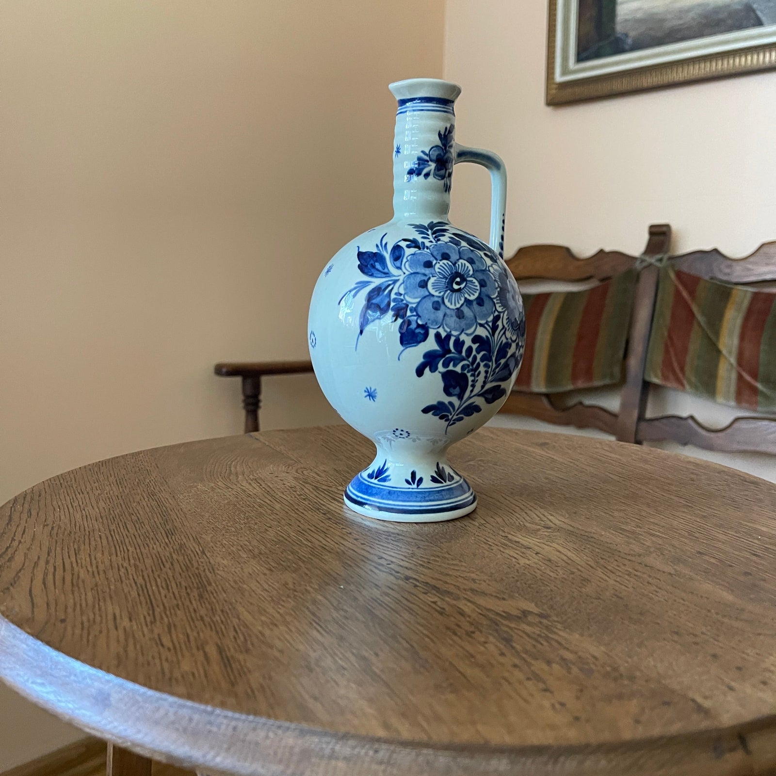 Blue and white floral-patterned vase on a wooden table with a chair and striped cushion in the background.