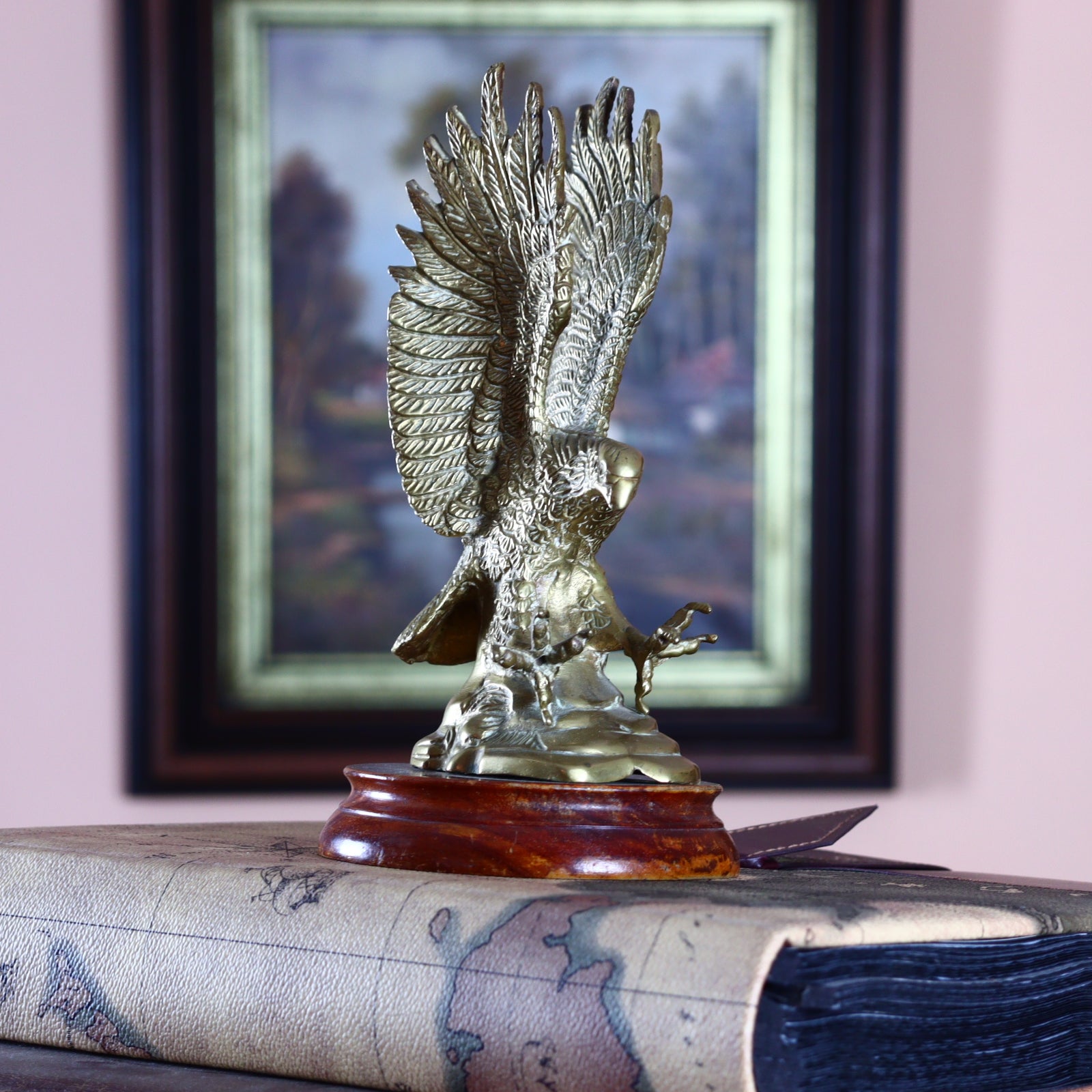 A brass eagle sculpture perched on a wooden pedestal, with a framed picture in the background.
