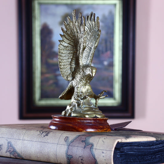 A brass eagle sculpture perched on a wooden pedestal, with a framed picture in the background.